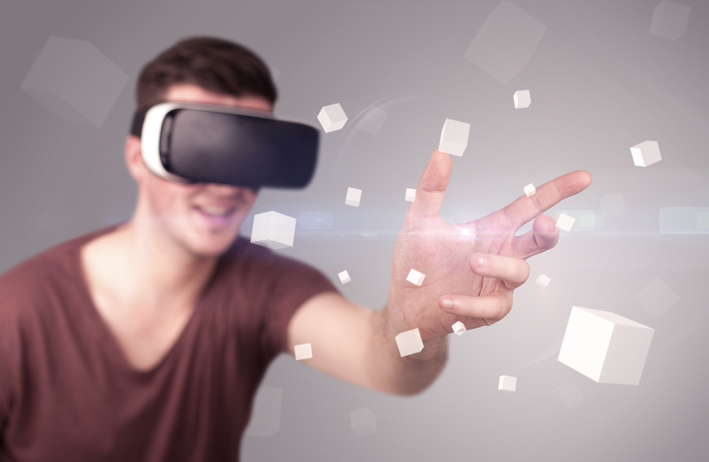 Young impressed man wearing virtual reality goggles with grey cubes around him